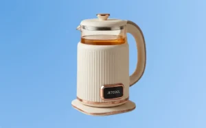 A white electric kettle with a glass lid, designed for brewing hot beverages efficiently.