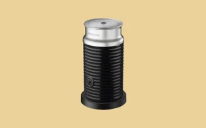 A black and silver milk frother positioned against a bright yellow background.